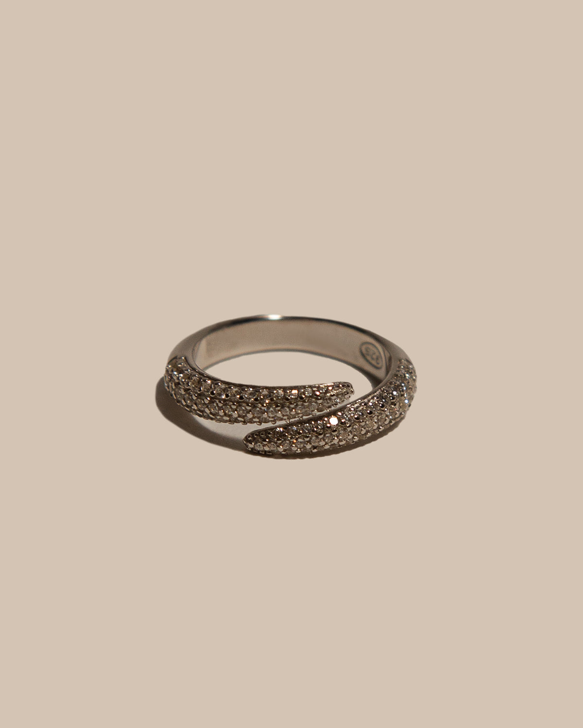 A silver wrap ring adorned with pavé-set brown gemstones, photographed on a solid beige background.