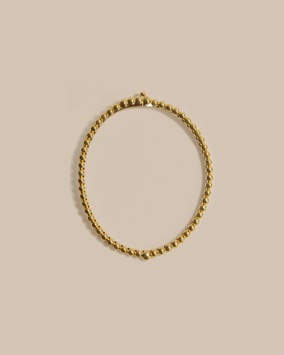 A gold-toned beaded chain necklace arranged in a loose oval on a solid beige background.