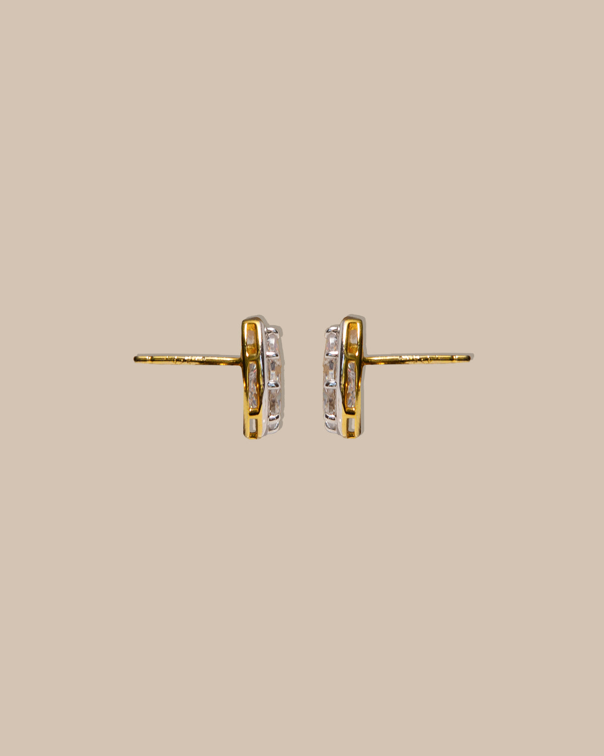 A pair of gold hoop earrings with a clear gemstone channel set on a solid beige background.